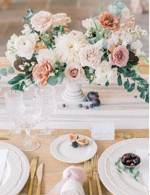 Elegant floral centerpiece with pink and white flowers, set on a dining table with plates, glasses, and cutlery.