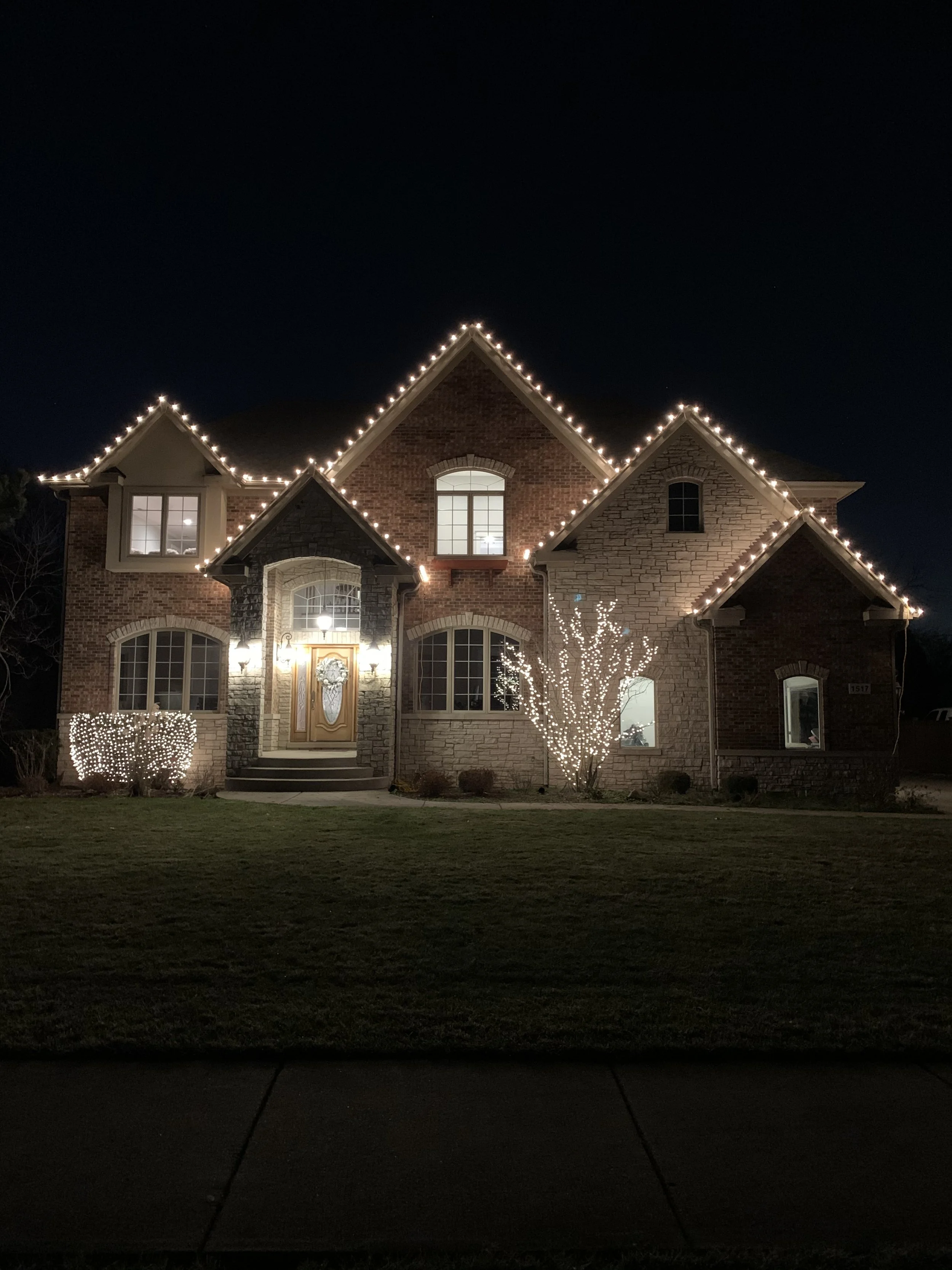 A large brick and stone house decorated with Christmas lights at night.