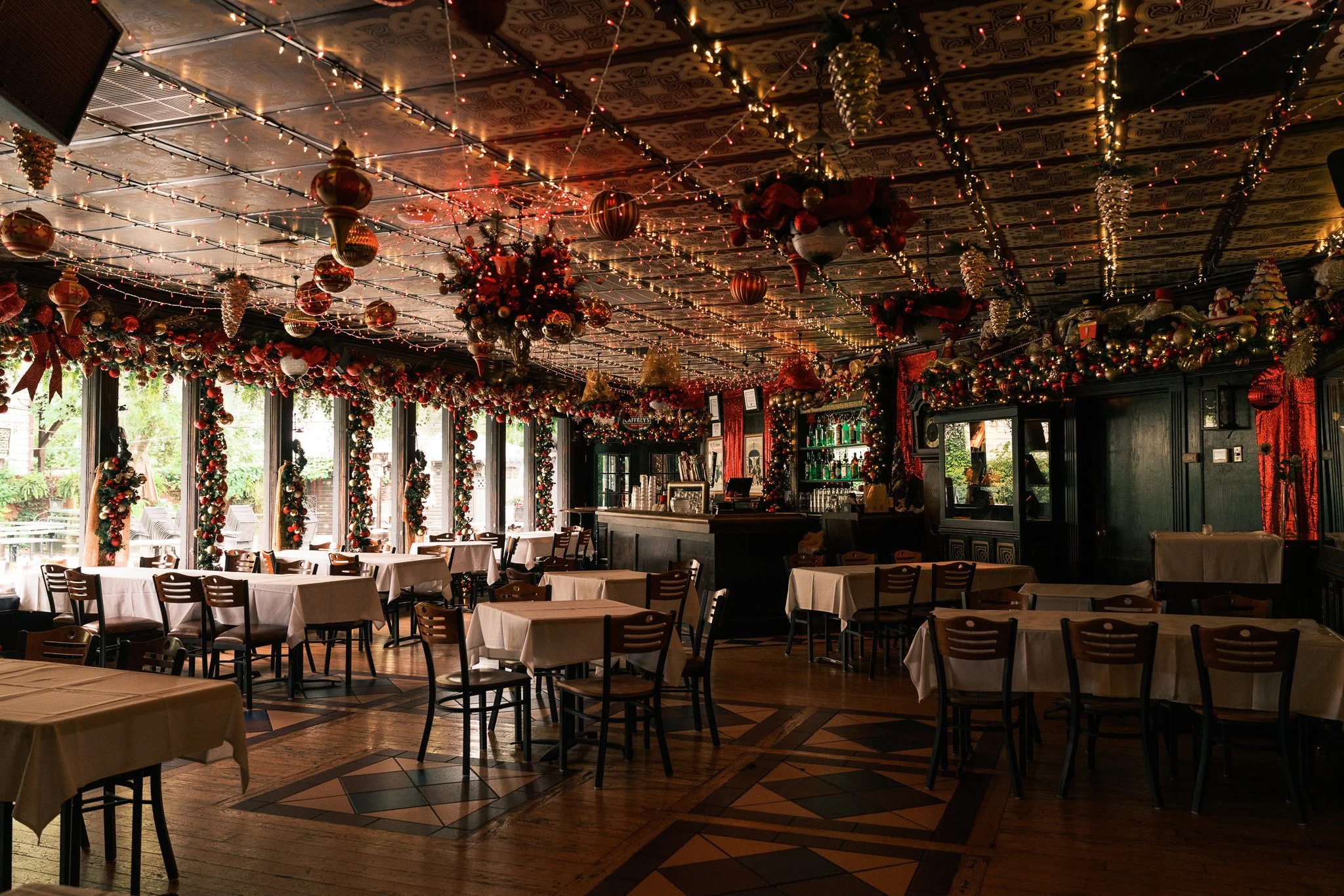 A restaurant decorated for Christmas with ornaments, garlands, and fairy lights hanging from the ceiling and around the windows, which are letting in natural light.