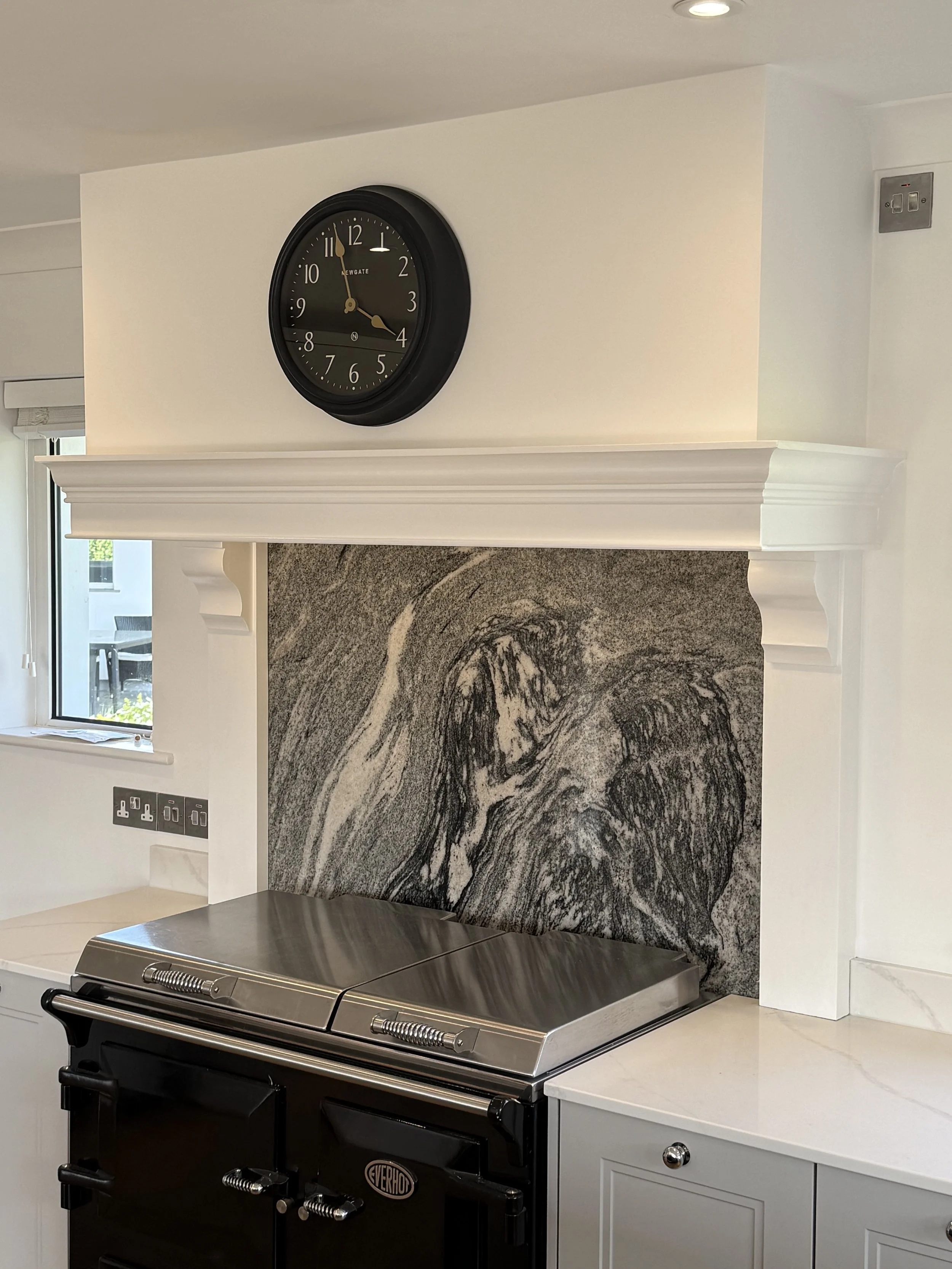 A black round wall clock shows 11:18 above a kitchen stove with a gray abstract stone backsplash and white cabinetry.