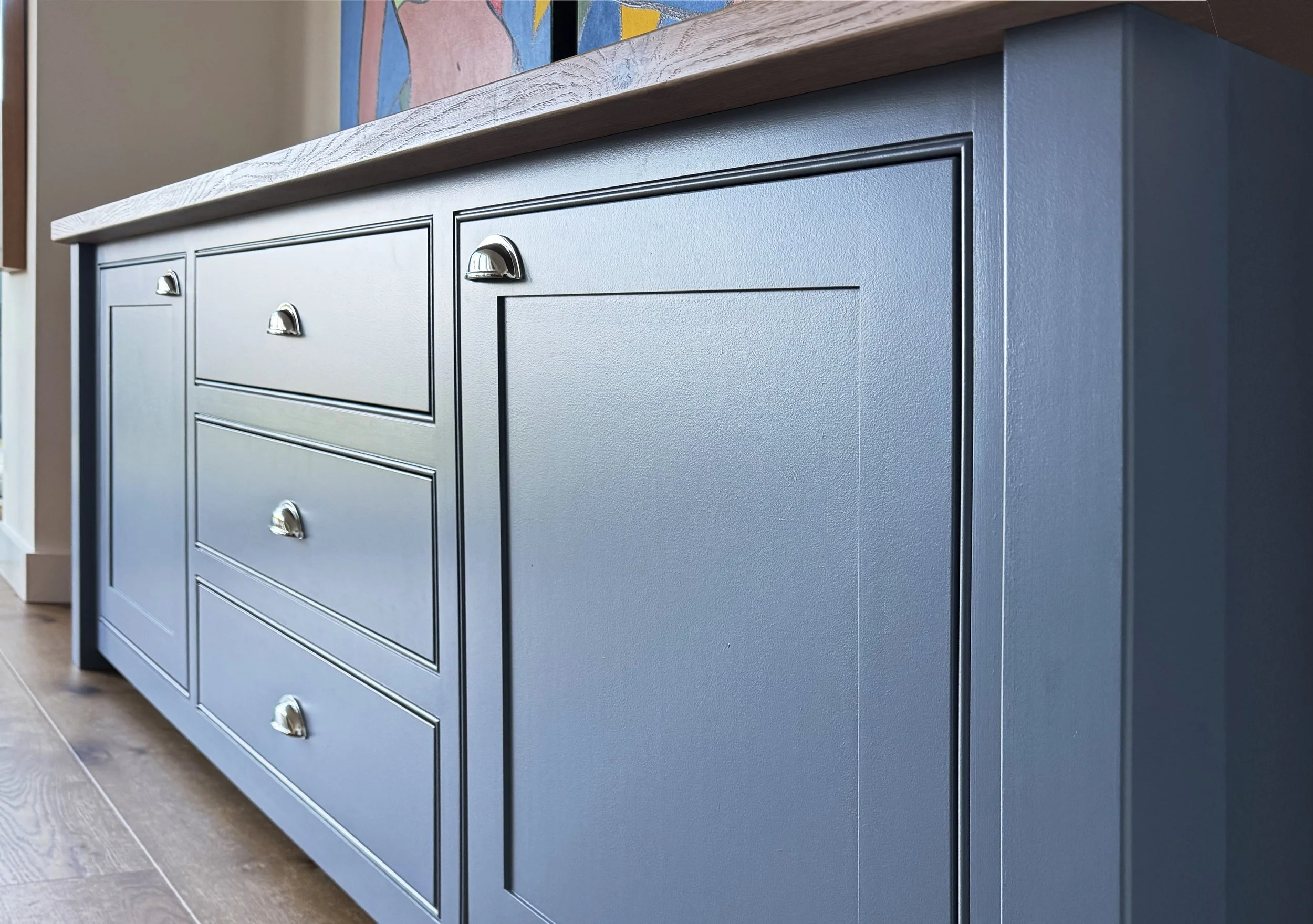 A blue wooden sideboard with three drawers and a cabinet door, topped with a light-colored wooden surface, in a room with wooden flooring.