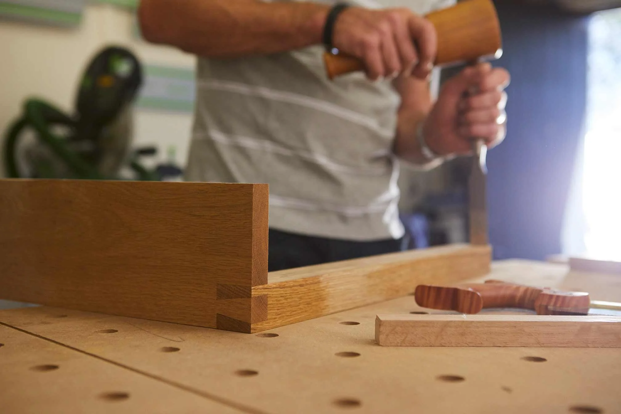 Person assembling a wooden furniture piece at a workbench with woodworking tools.