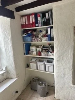 Shelves filled with binders, boxes, jars, and miscellaneous items near a window in a room with white textured walls.