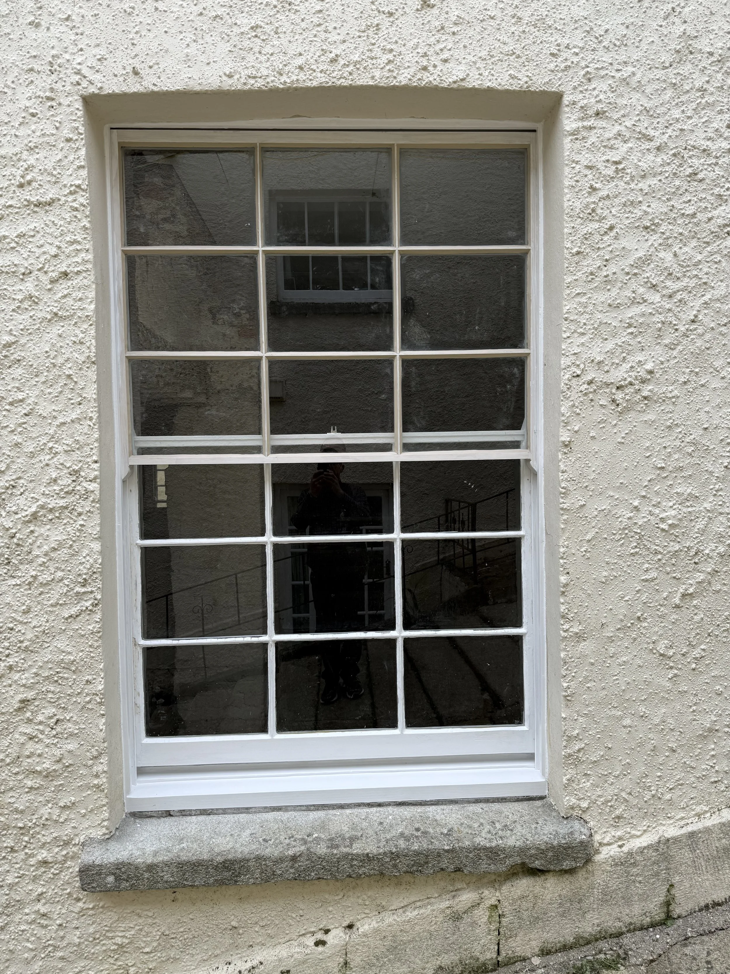 A white-framed window with 12 panes set into a textured off-white wall, with a stone sill at the base.