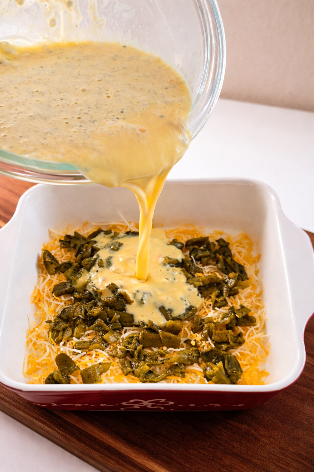 Egg mixture being poured over Hatch green chiles and cheese for breakfast casserole