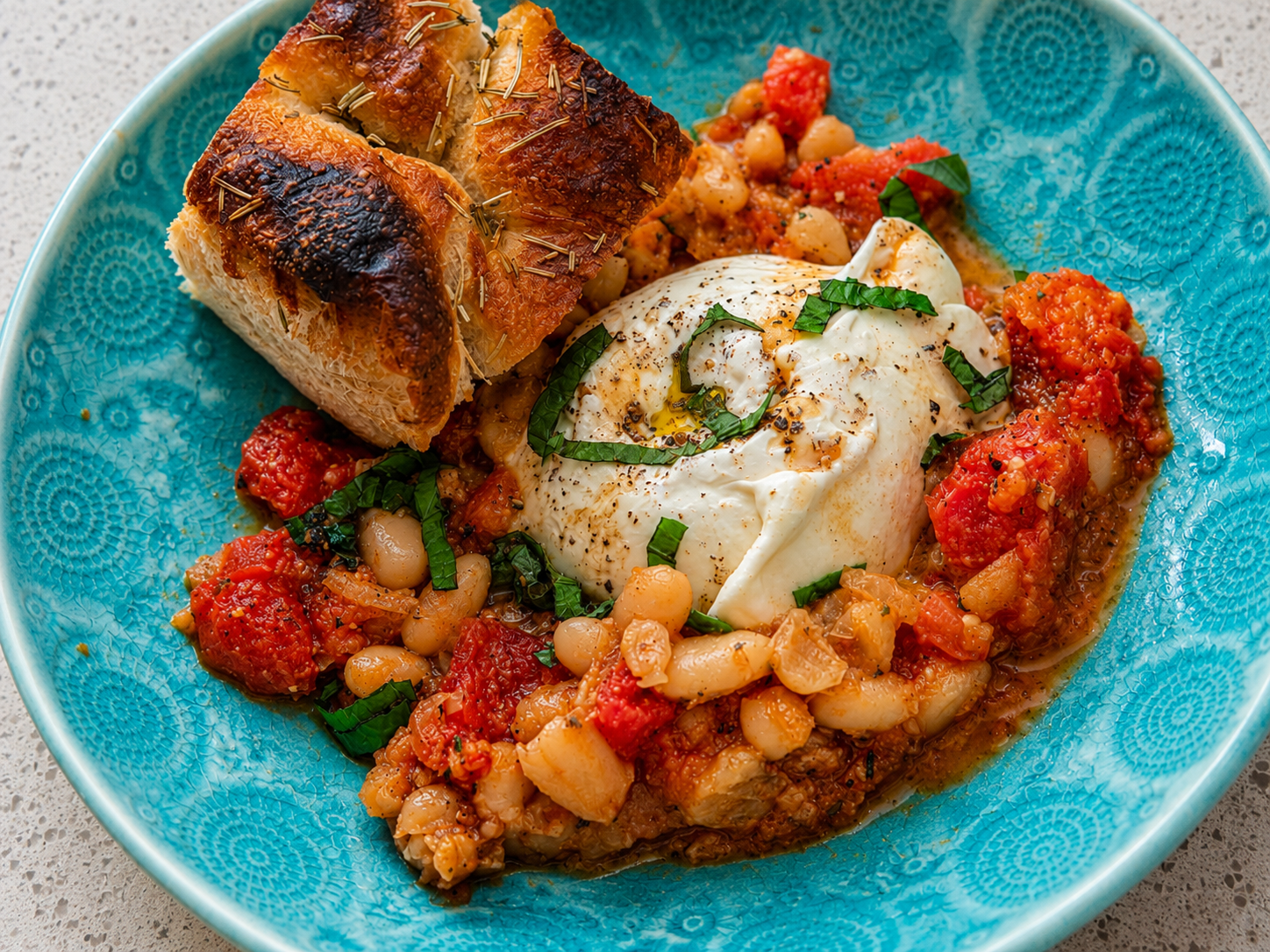 Creamy tomato white beans with burrata served with rosemary focaccia in a turquoise bowl