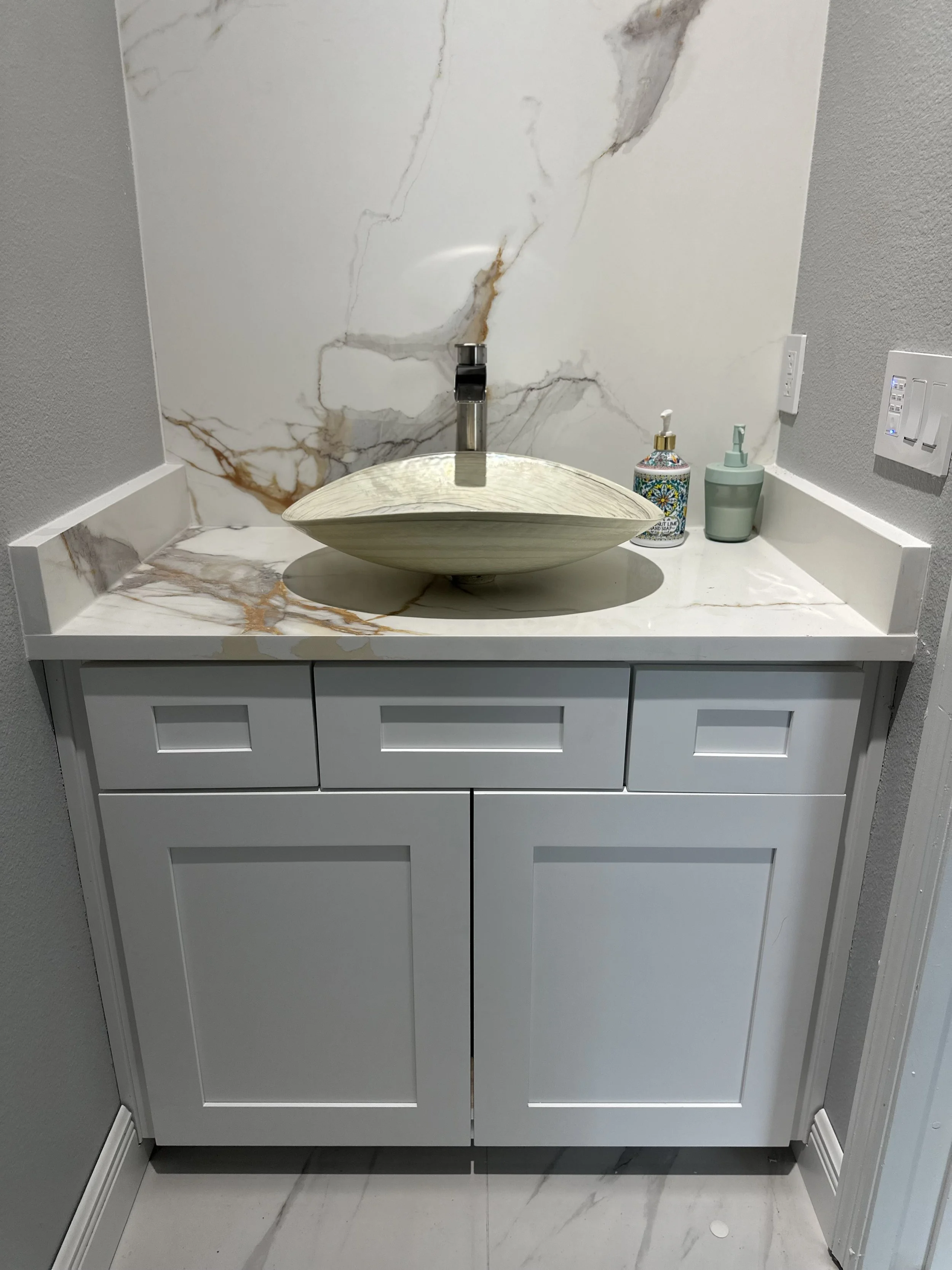 Bathroom vanity with a marble countertop, vessel sink, and soap dispensers.