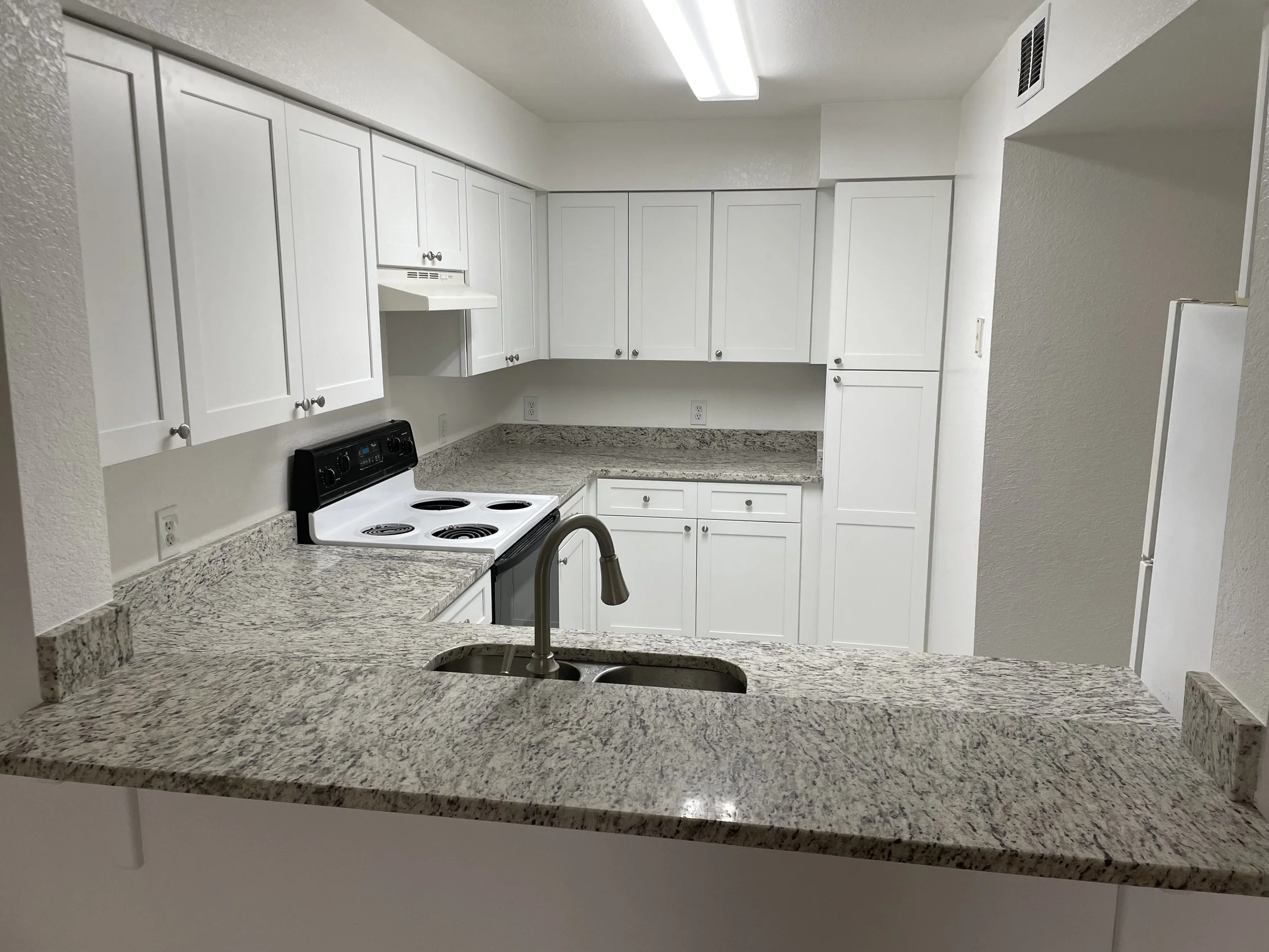 Kitchen with white cabinets, granite countertops, a white stove, and a kitchen sink.