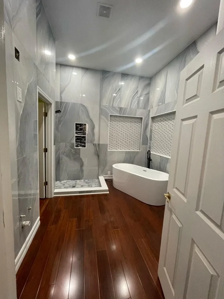 Bathroom with marble walls, a walk-in shower with mosaic tile, a white freestanding bathtub, and wood flooring.
