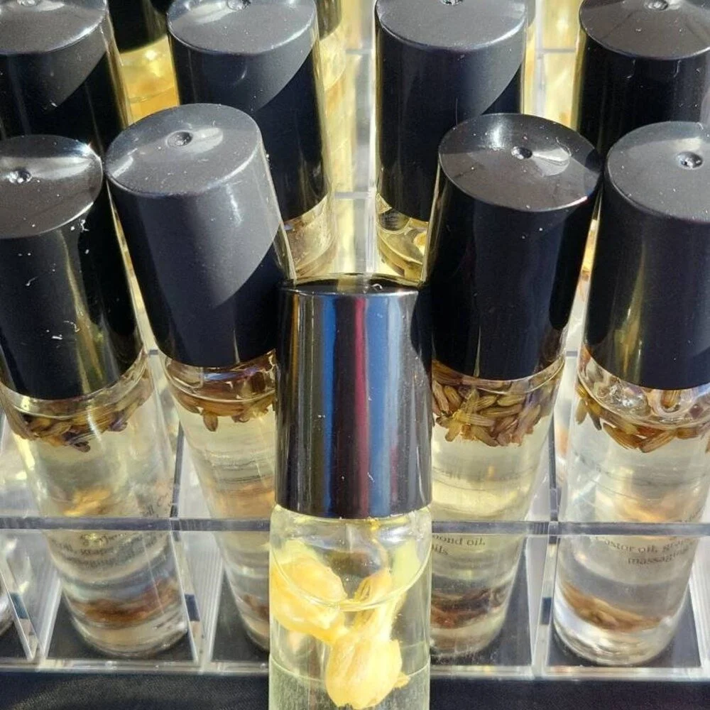 Close-up of several small bottles filled with golden yellow essential oils and a few attached dried herbs or flowers, with black caps, arranged in a display stand.