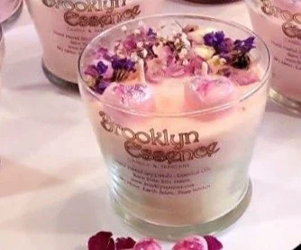 A glass candle holder with a pink candle and flower petals inside, labeled 'Brooklyn Candle'.