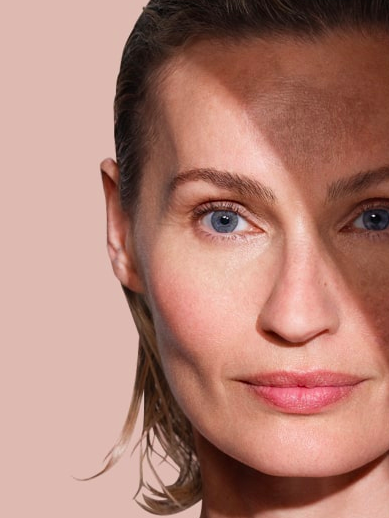 Close-up of a woman's face with blue eyes and light makeup against a plain background.
