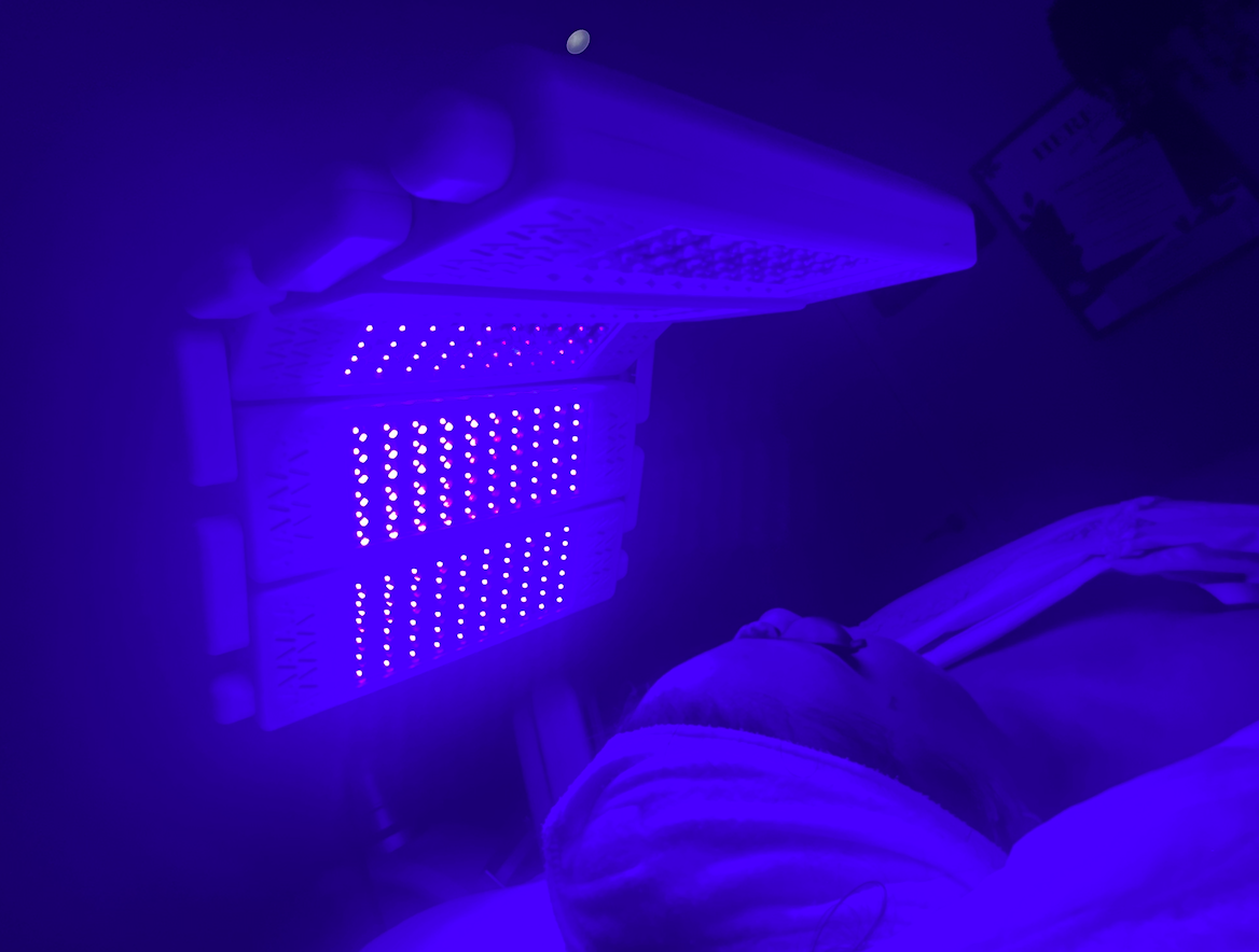Person lying in bed under blue light from a UV therapy device.