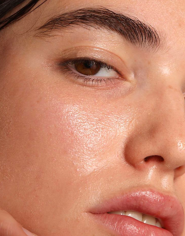 Close-up of a woman's face showing smooth, glowing skin, well-groomed eyebrows, and slightly parted lips.