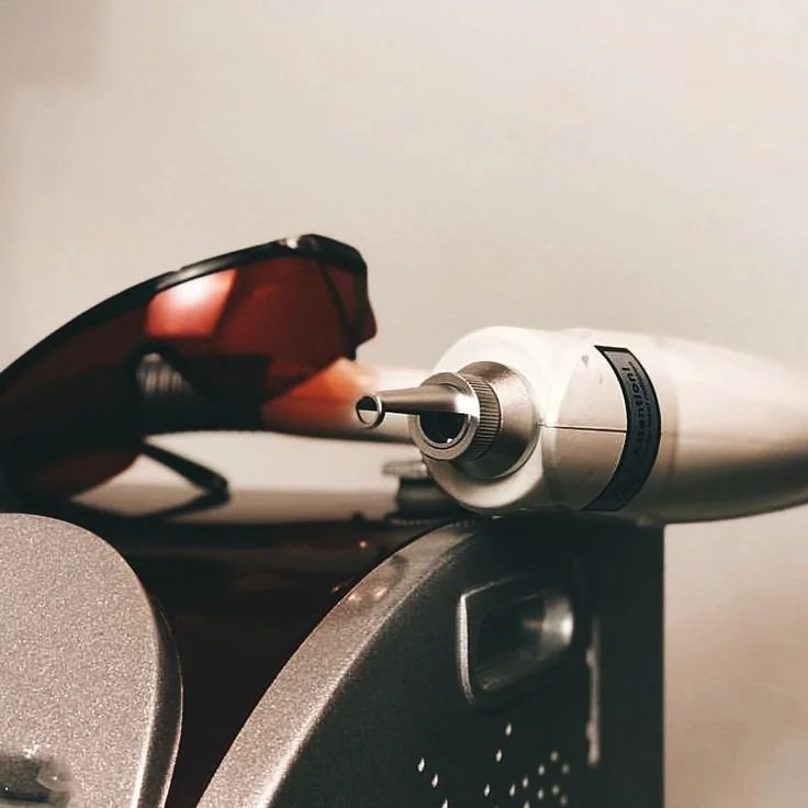 Close-up of a turntable tonearm with a stylus resting on a surface, alongside a pair of sunglasses with red-tinted lenses.