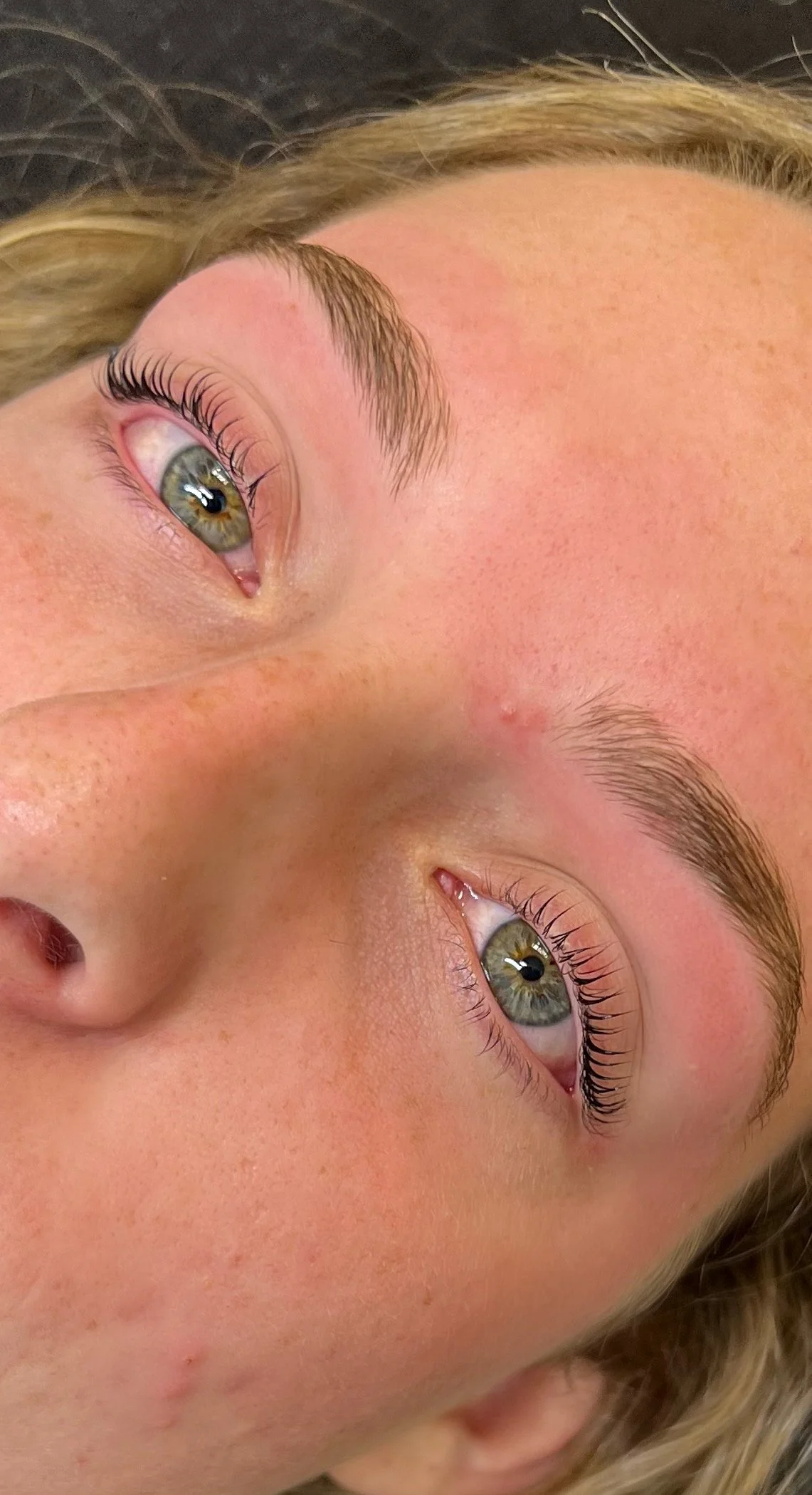 Close-up of a person's face showing green eyes, light skin, and eyebrows with a natural shape.