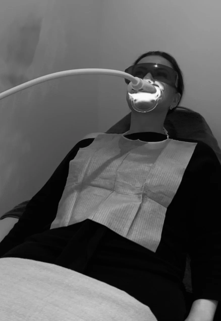 A woman lying down with her mouth connected to a medical device, wearing protective eyewear and a bib, in a medical setting.
