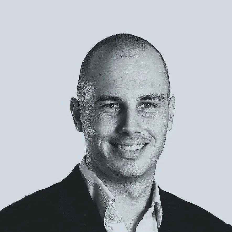 Black and white portrait of a man with a buzz cut, wearing a collared shirt and blazer, smiling.