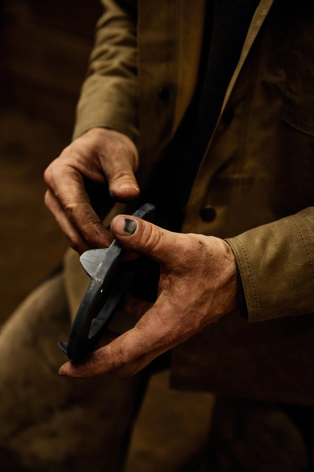 A person's hands, dirty and rough, holding a horseshoe.