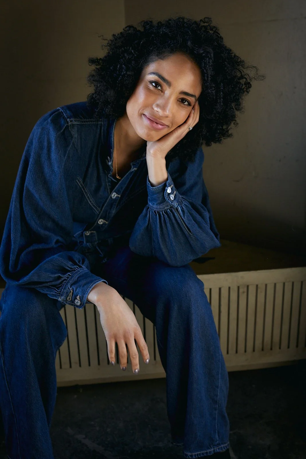 Model wearing a denim jumper with hand on face
