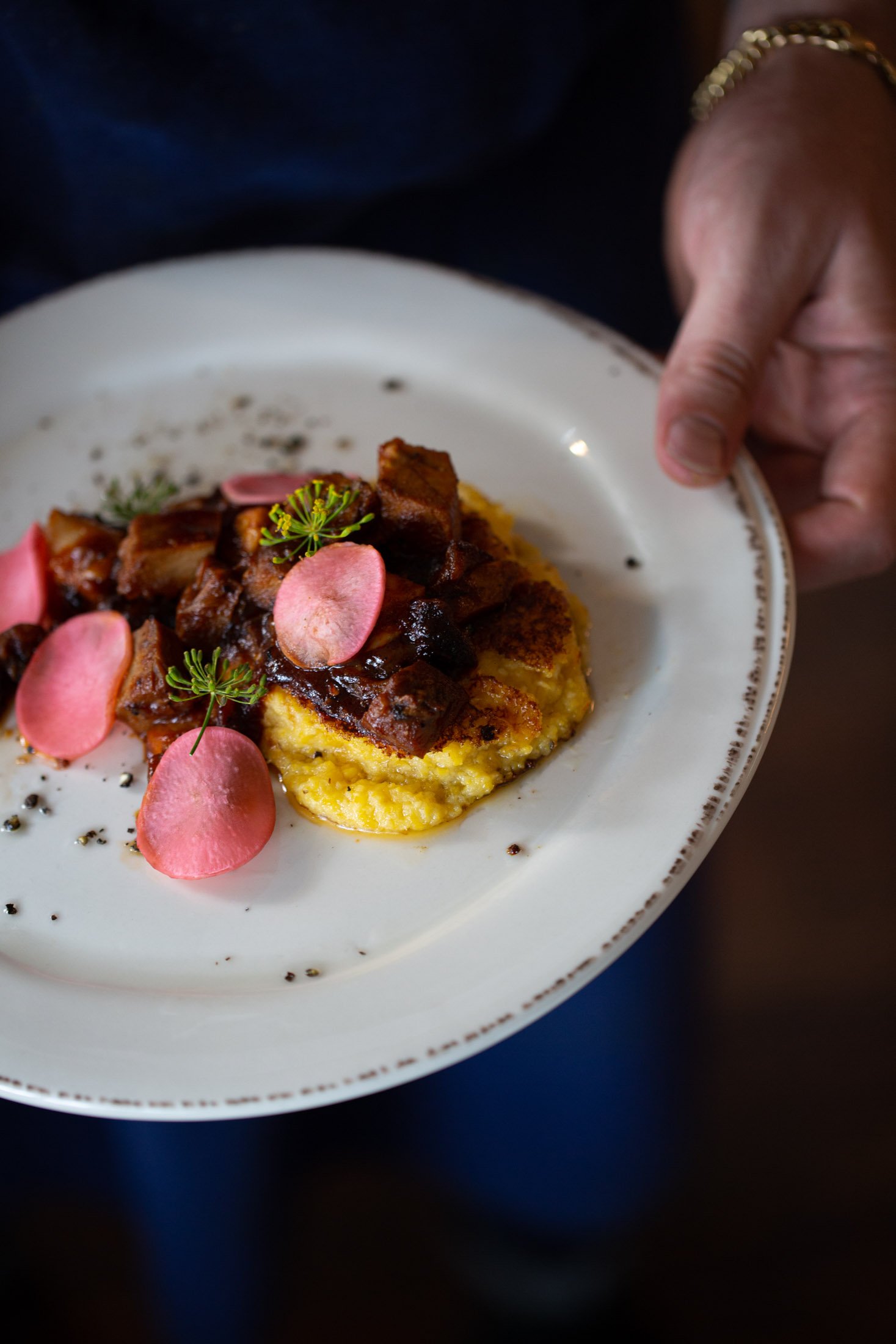 Chef holding a plate of short ribs and grits with picked radishes at The Regional restaurant in Fort Collins Colorado