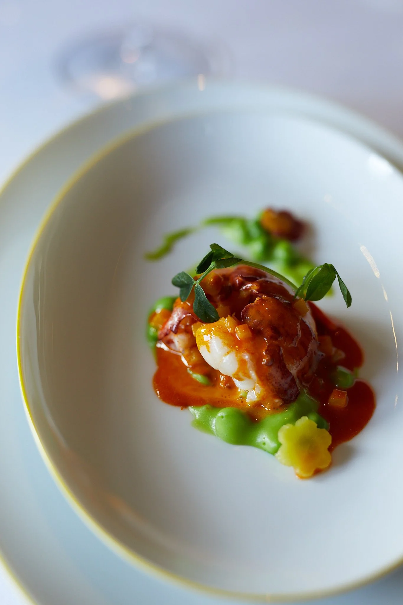 A plated dish with a piece of seafood topped with a red sauce, garnished with green herbs and accompanied by vegetables  at the French Laundry.