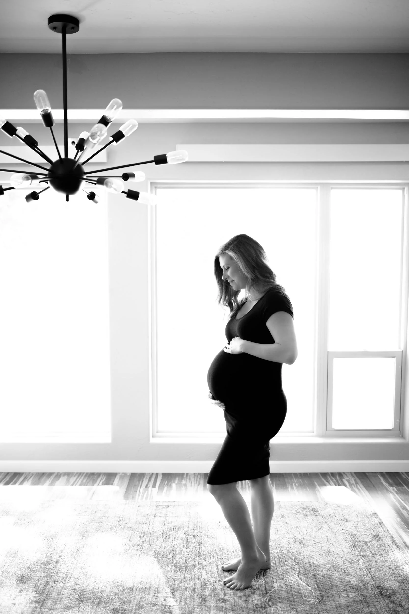 Black and white portrait of a pregnant woman in front of a large window