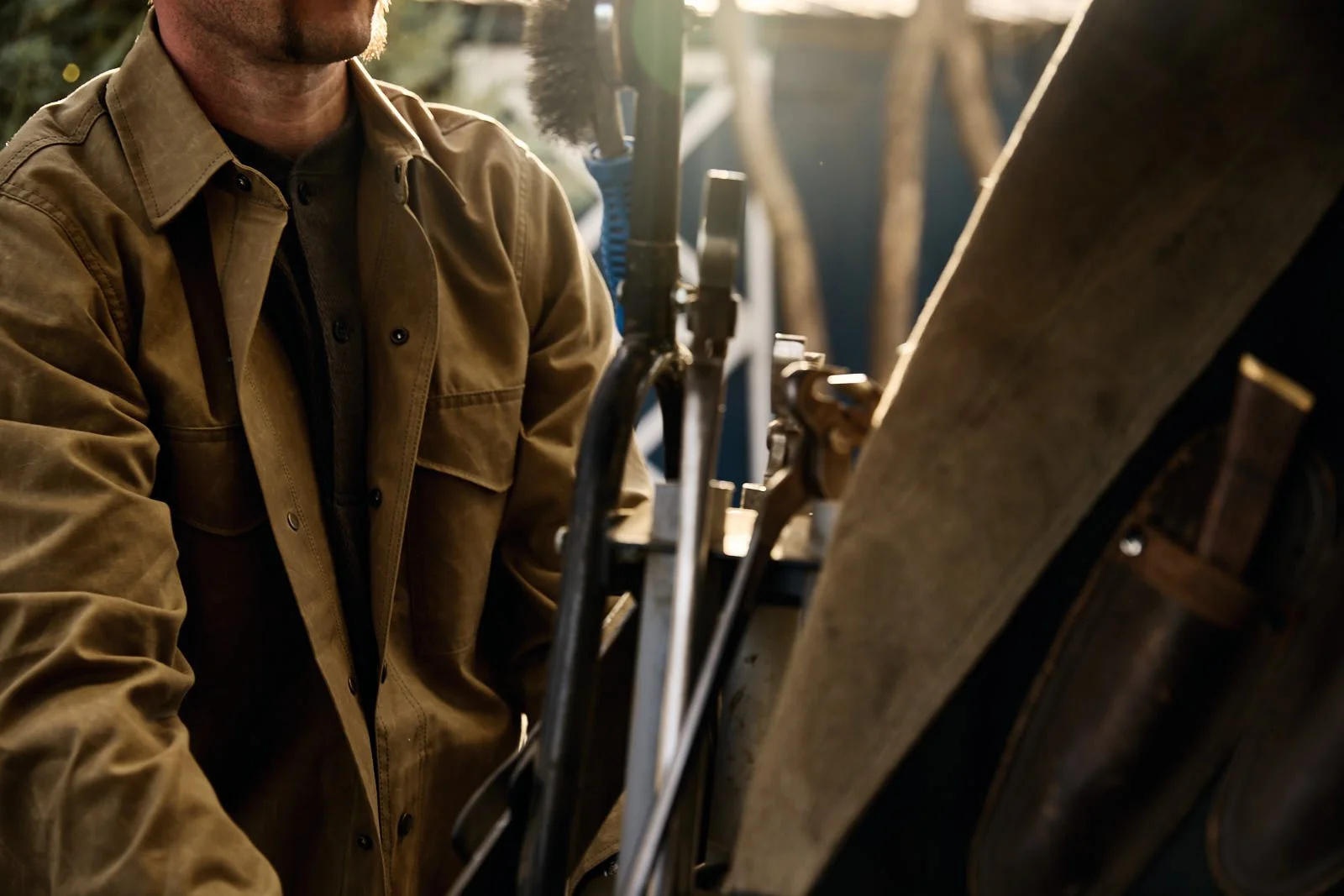 A person wearing a brown jacket working on a machine outdoors, with tools and equipment around.