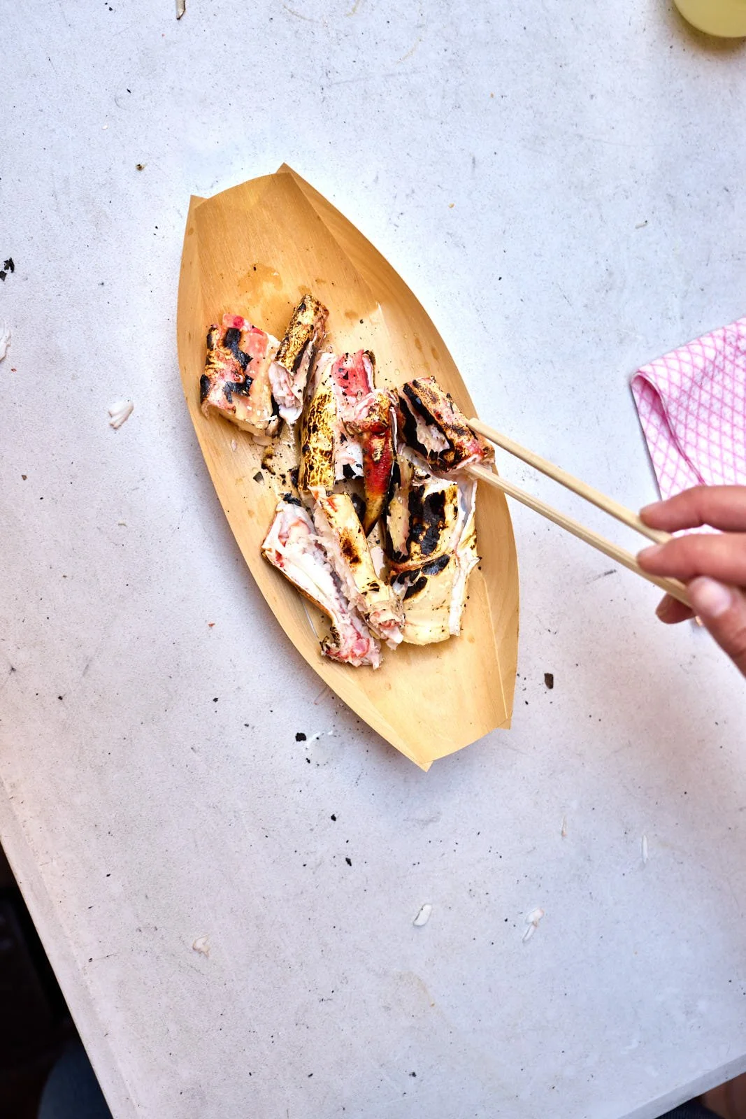 Grilled sushi rolls on a wooden plate, with a person's hand holding chopsticks, on a white countertop.