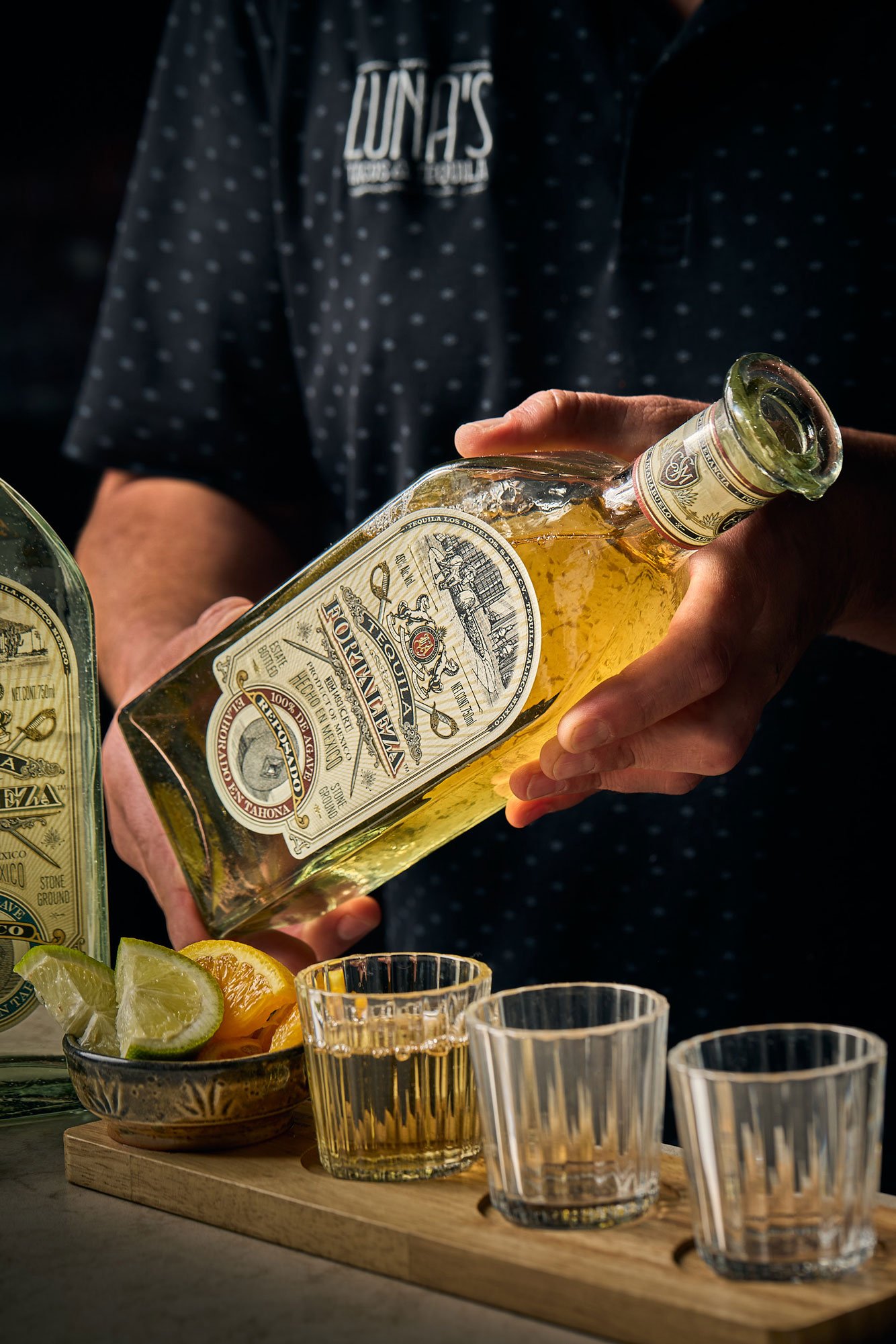 Bartender holding tequila bottle with a flight board of tequila