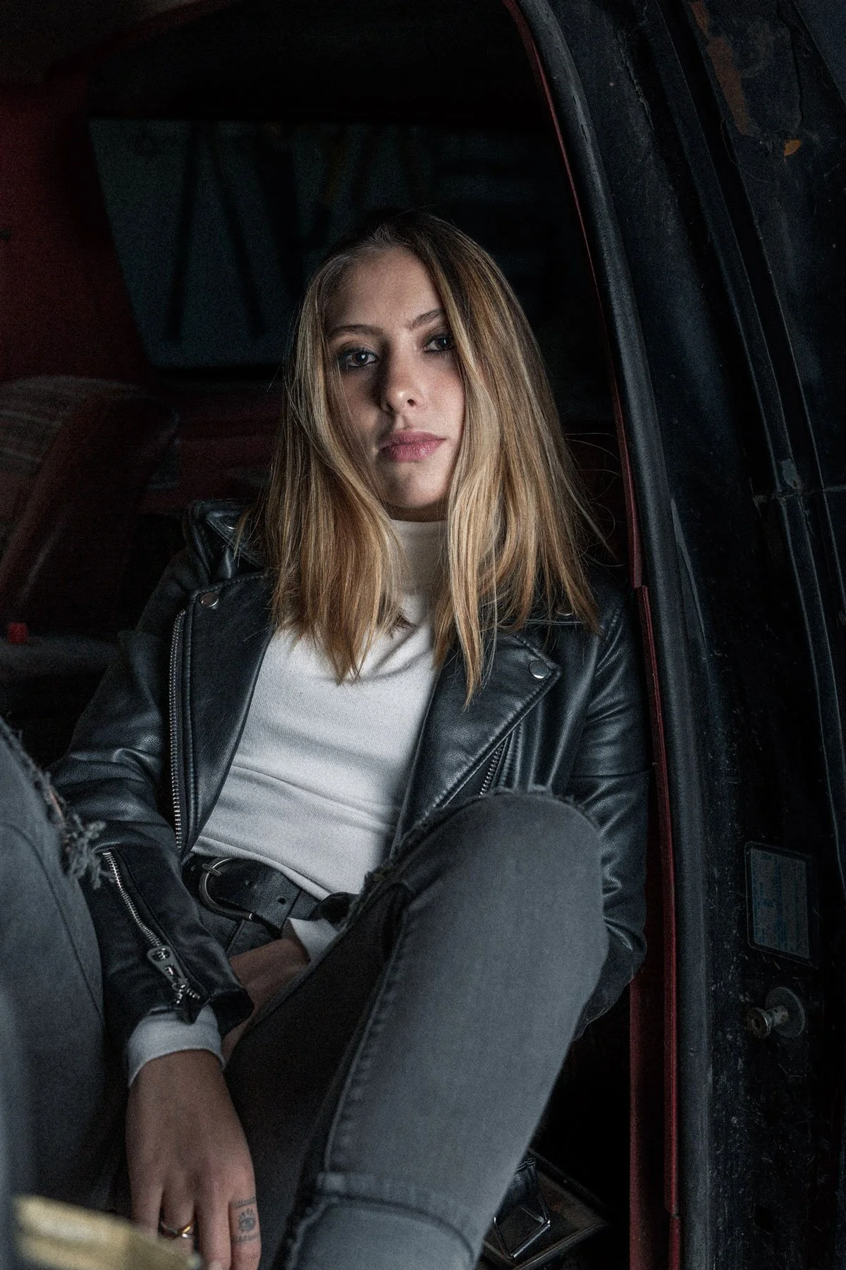 Model wearing black leather jacket seated in an old Ford Bronco