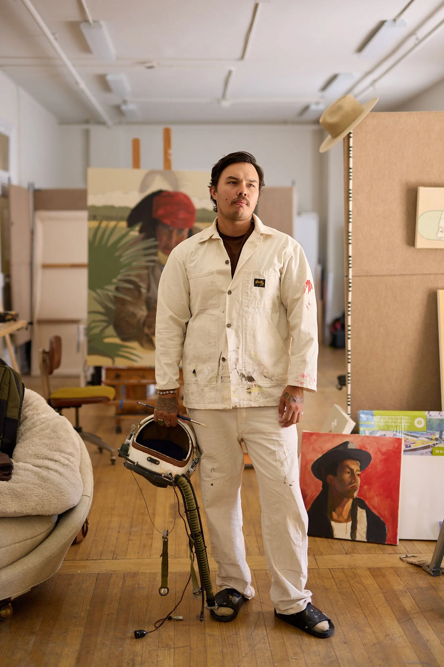 Portrait of artist George "Ofuskie" Alexander standing in his Santa Fe, NM studio with an astronaut helmet