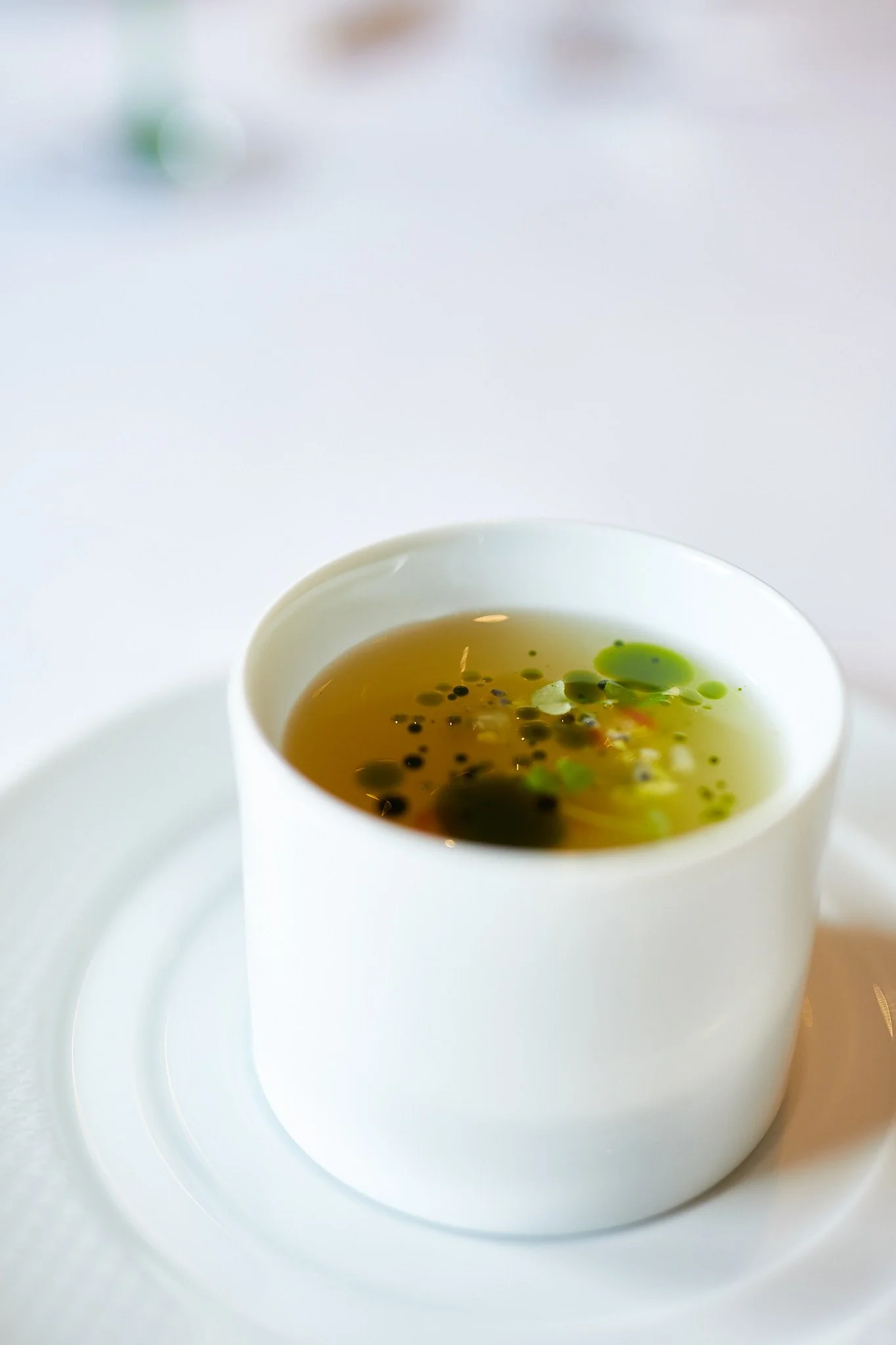 A white cup filled with consomme on a white saucer.