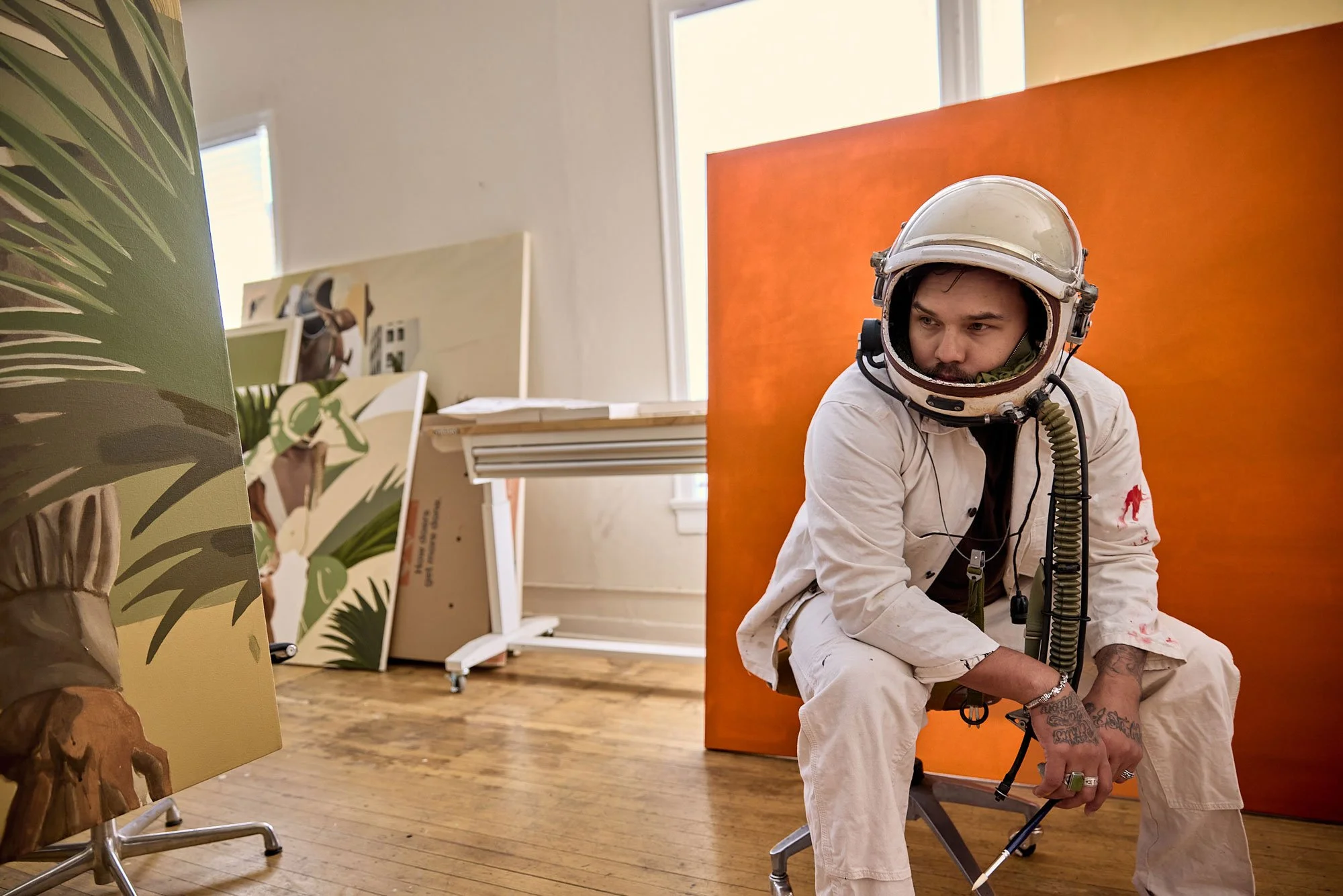 Portrait of artist George "Ofuskie" Alexander wearing an astronaut helmet in front of an orange painting