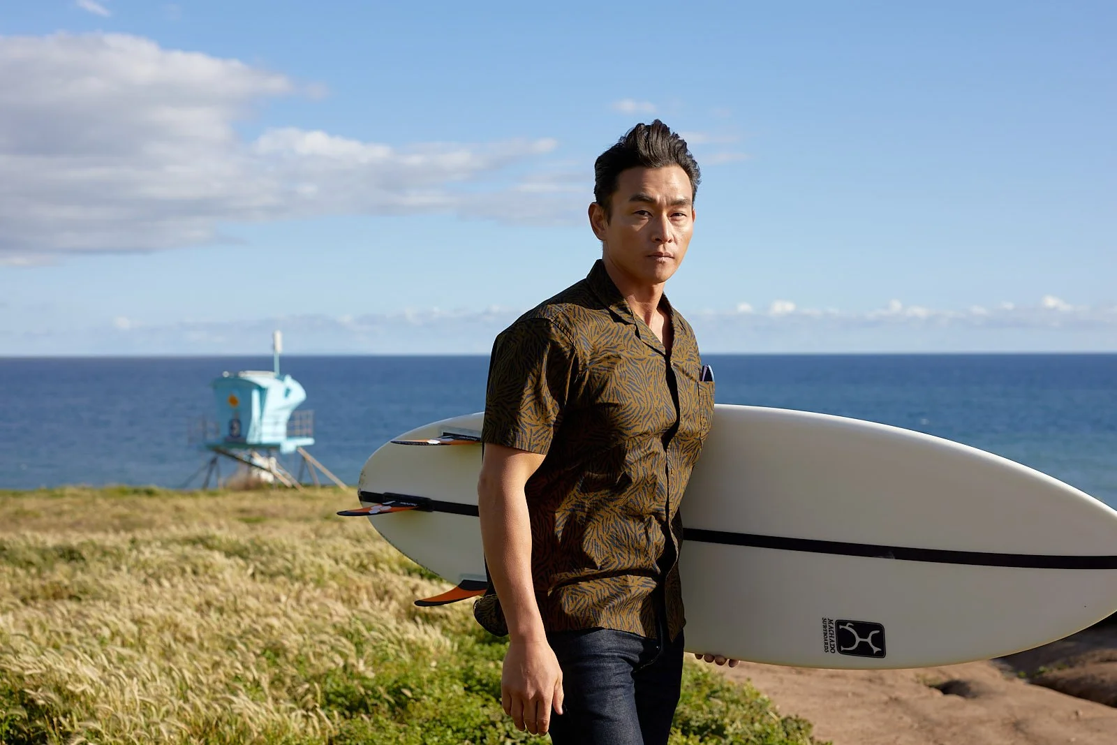 Man in street clothes standing with surfboard on the California coast