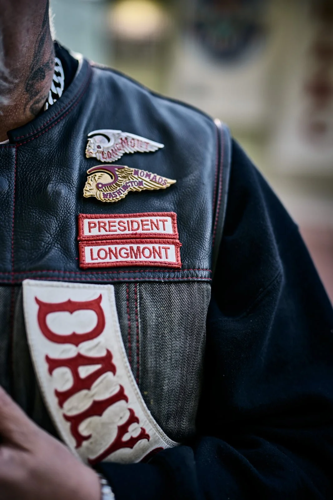 Close-up of a black leather vest with patches and badges, including two wing-shaped pins