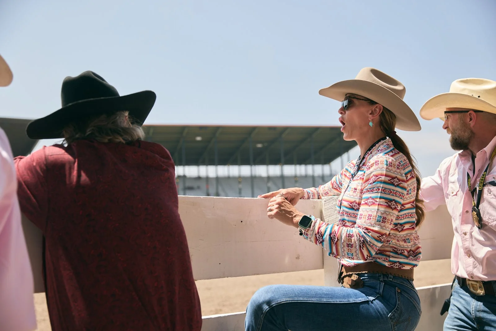 People at a racetrack, some wearing cowboy hats yelling under a sunny sky.
