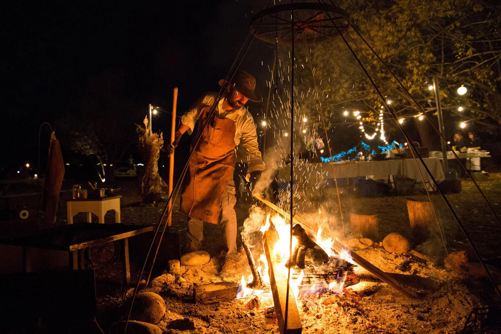 Chef attending to an open outdoor cooking fire at night