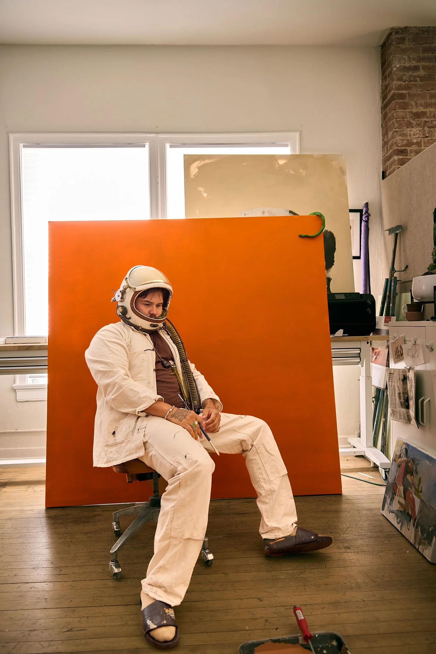 Artist George Alexander wearing astronaut helmet in front of an orange painting in his Santa Fe studio