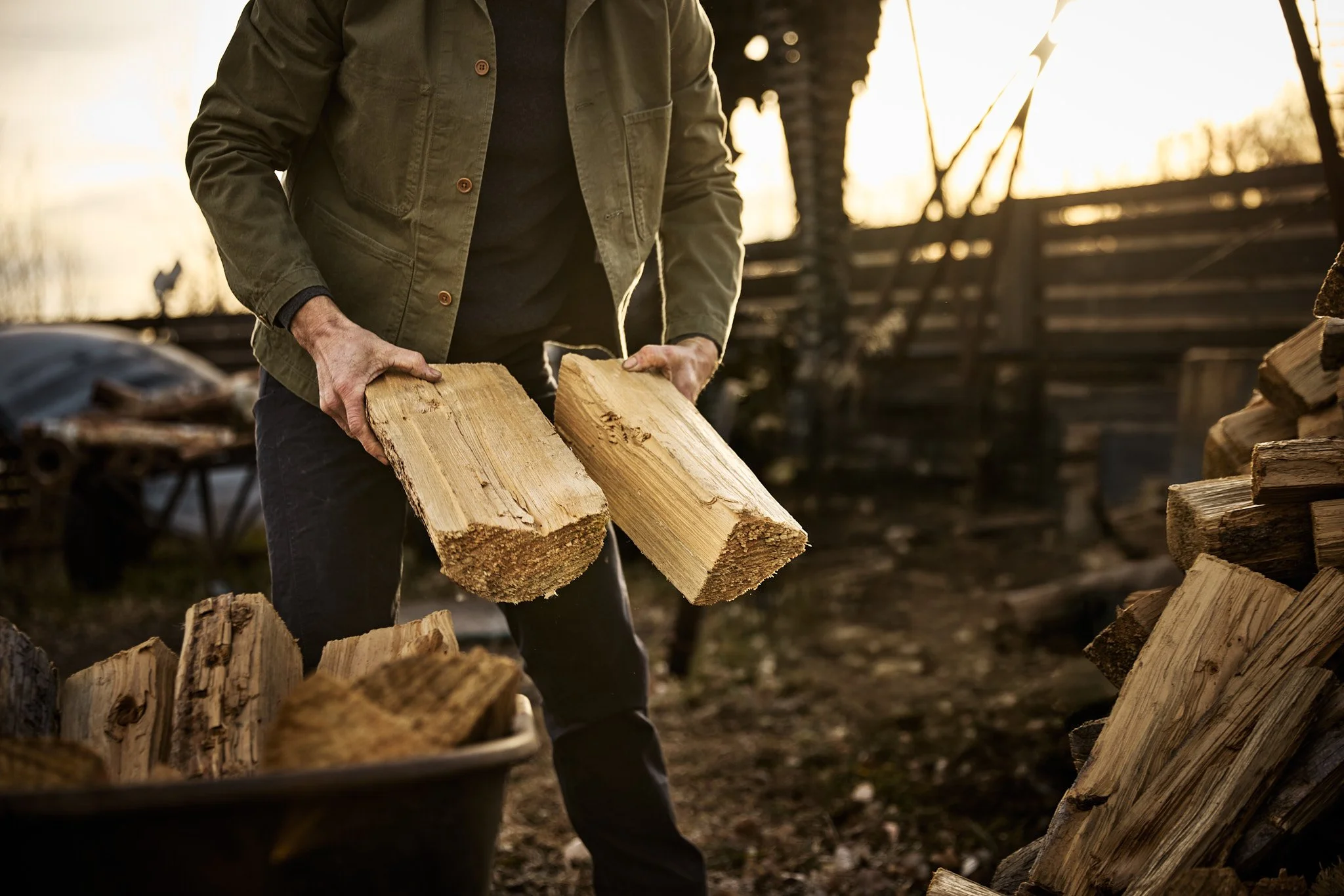 Person stacking firewood outdoors at sunrise