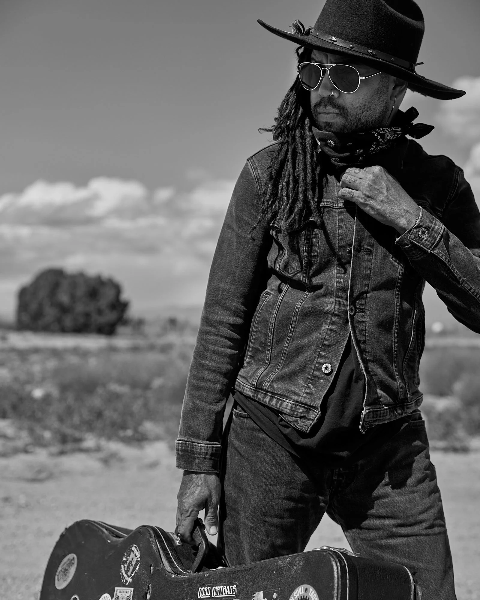 Black and white portrait of a musician standing outside with guitar case in hand