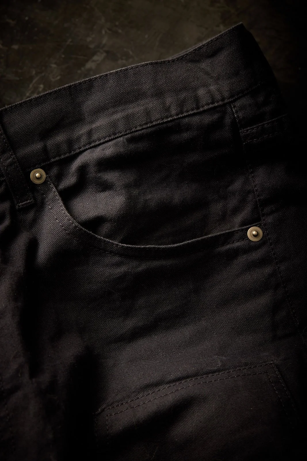 Close-up of black fabric pants with a front pocket and metal rivets.