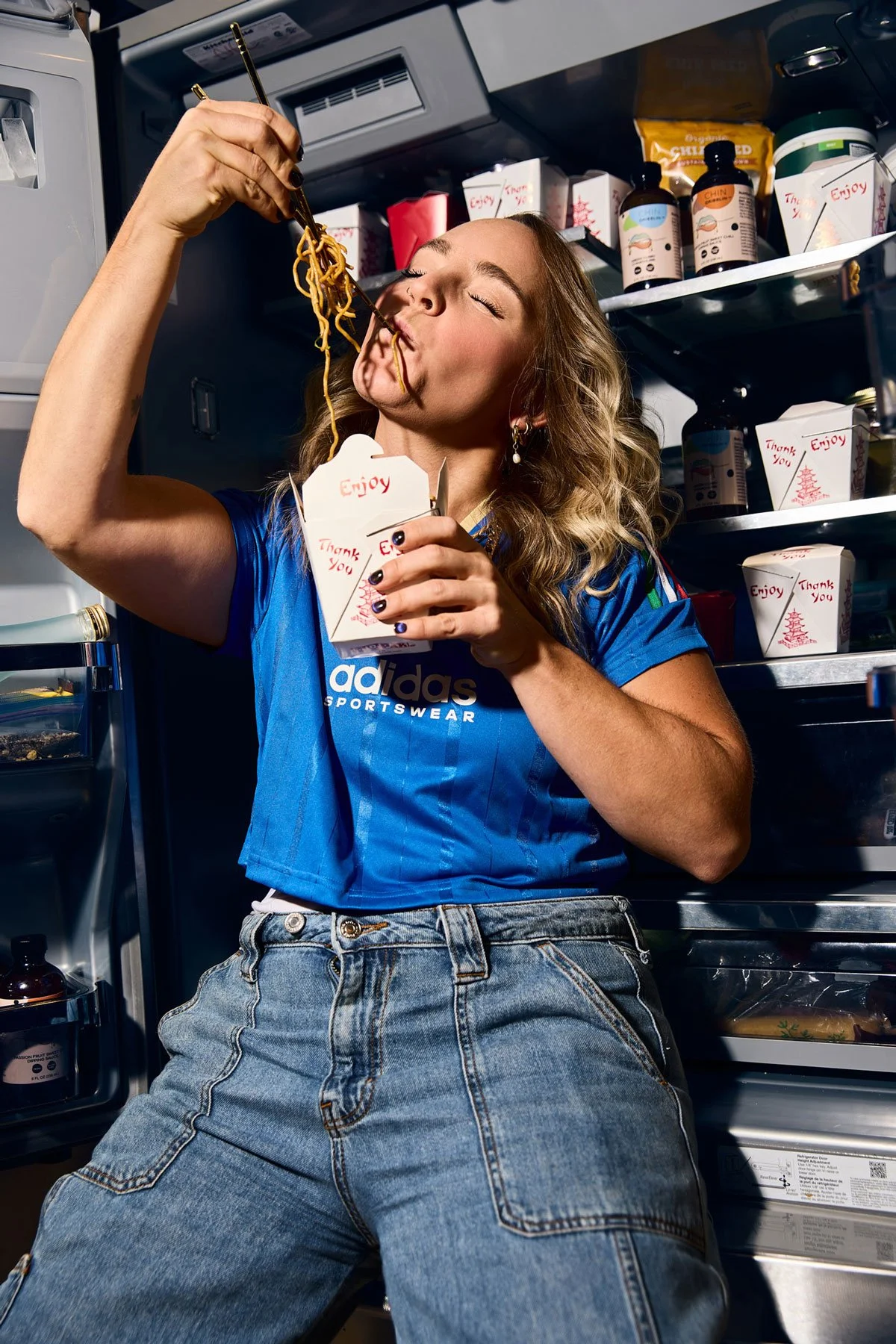 Ali Schlichter eating taking out while sitting in an open refrigerator