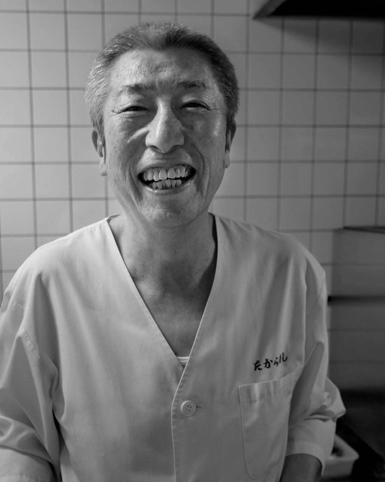 A smiling sushi chef wearing traditional restaurant shirt in black and white
