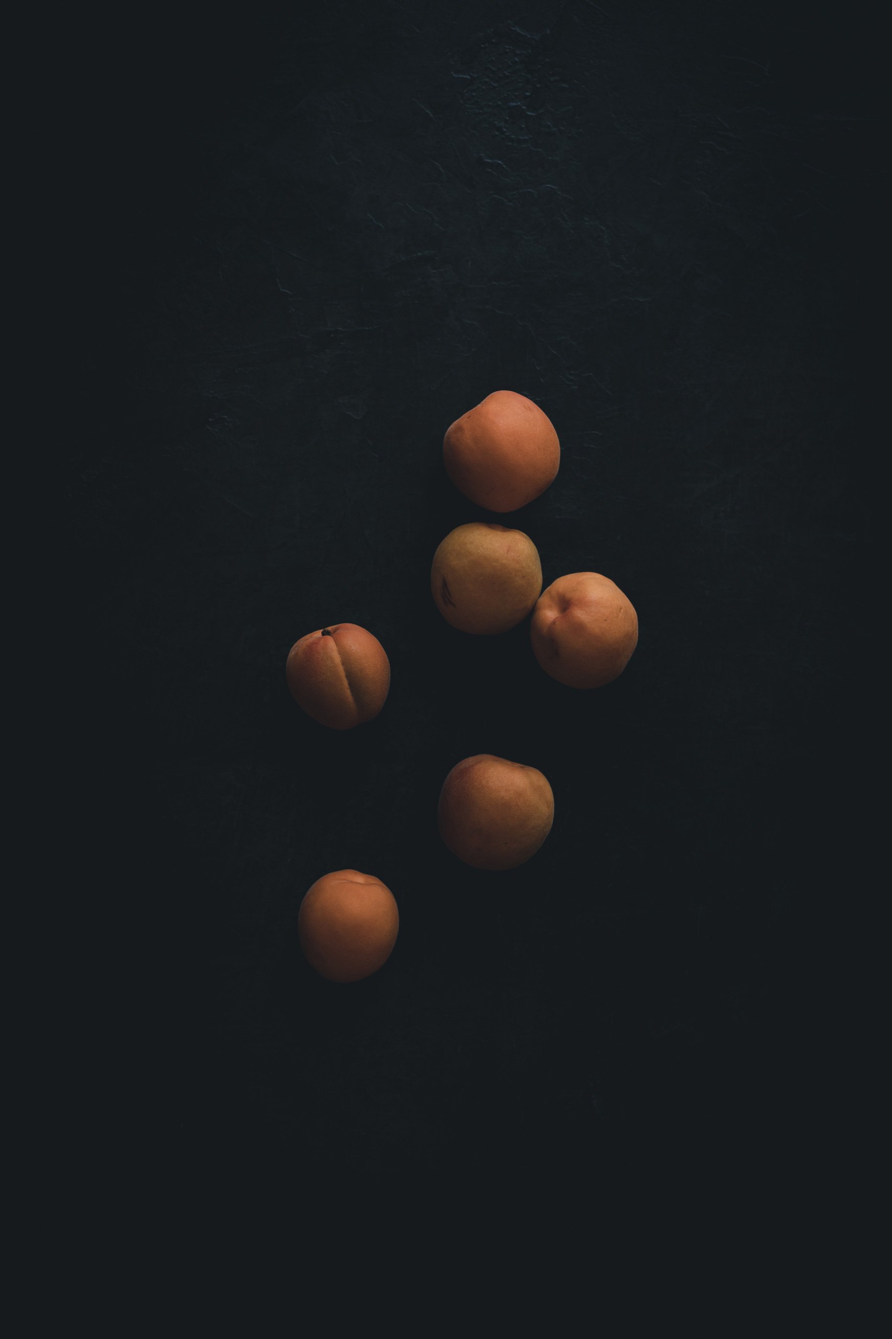 Six peaches arranged on a dark surface with minimal lighting.