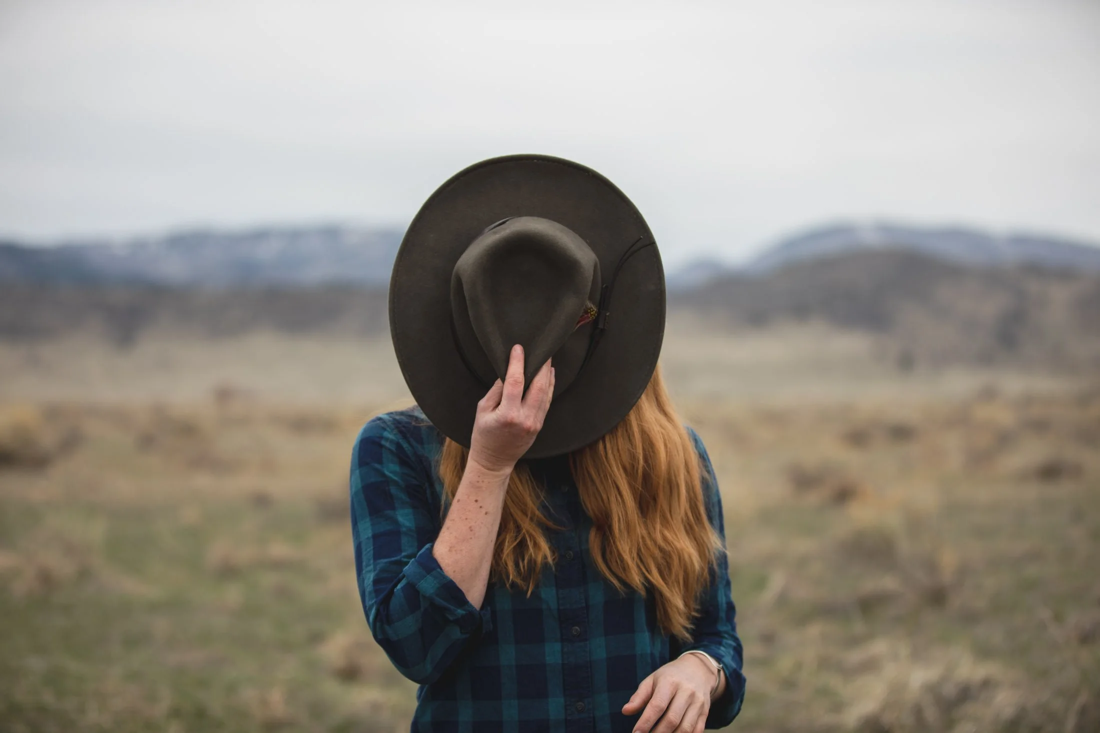 Woman posing with Filson hat covering her face in front of Rocky Mountains