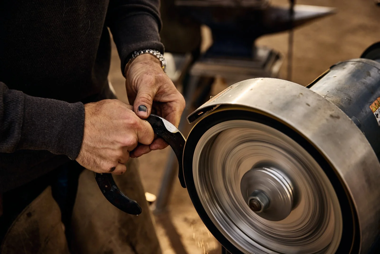 A person uses a grinding wheel to sharpen or shape a metal horseshoe with sparks flying off.