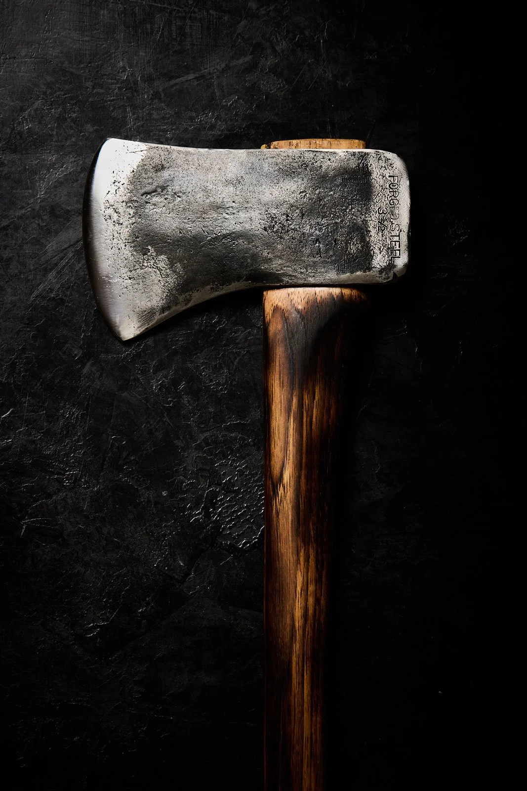 A weathered axe with a metal head and a wooden handle resting on a dark textured surface.