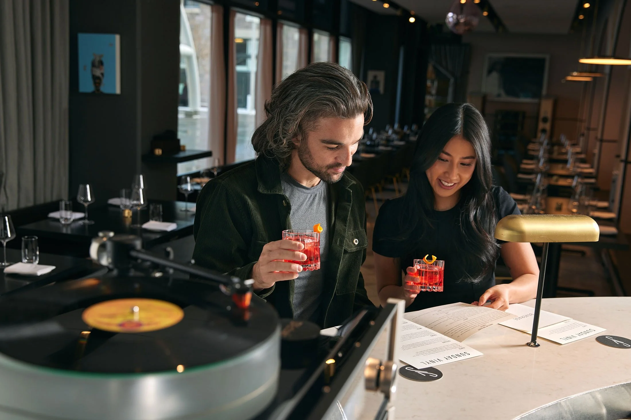 Couple enjoying negronis and looking at menus at Sunday Vinyl in Denver Colorado