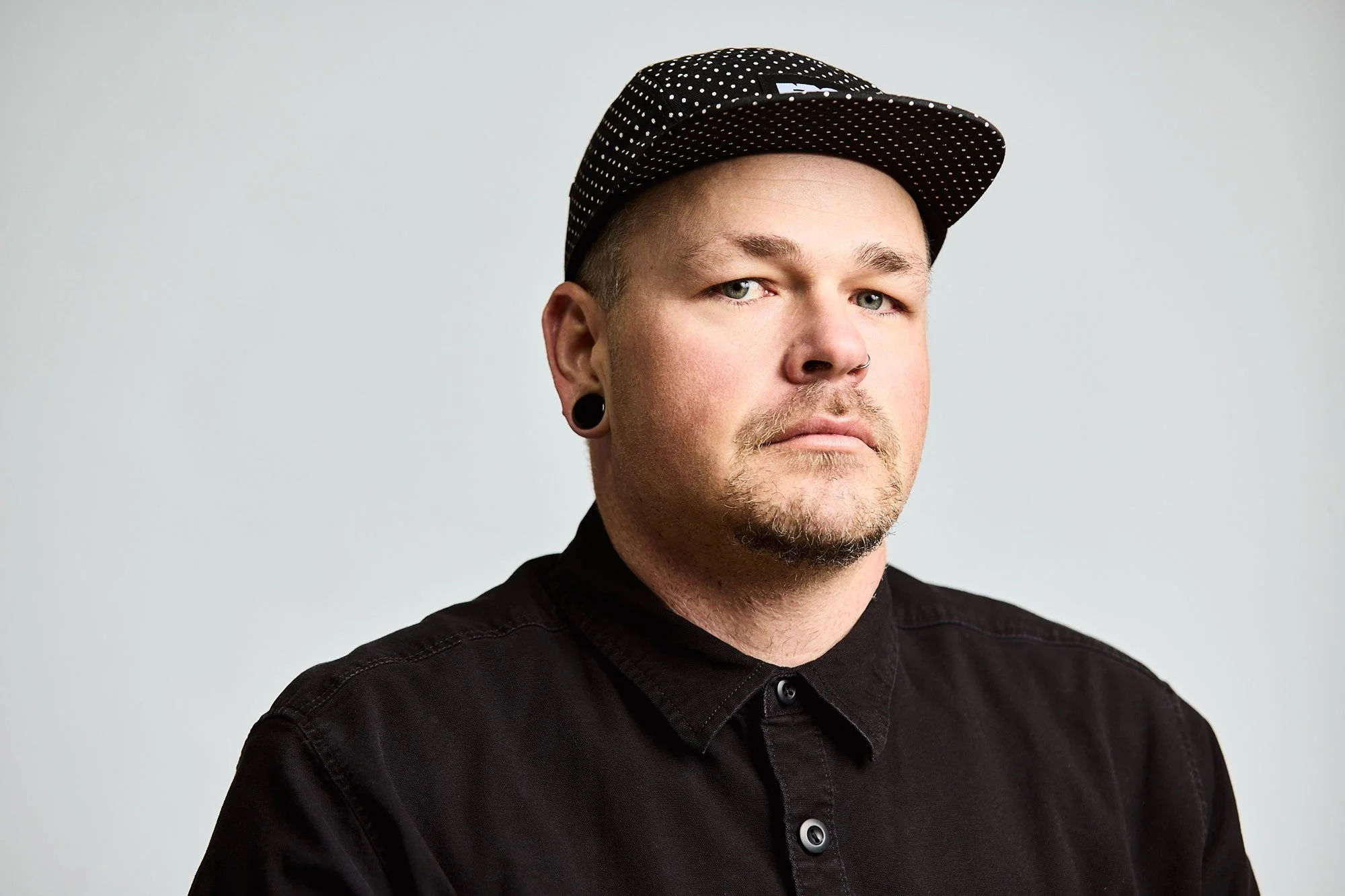 Headshot of a man in black wearing a skate style hat